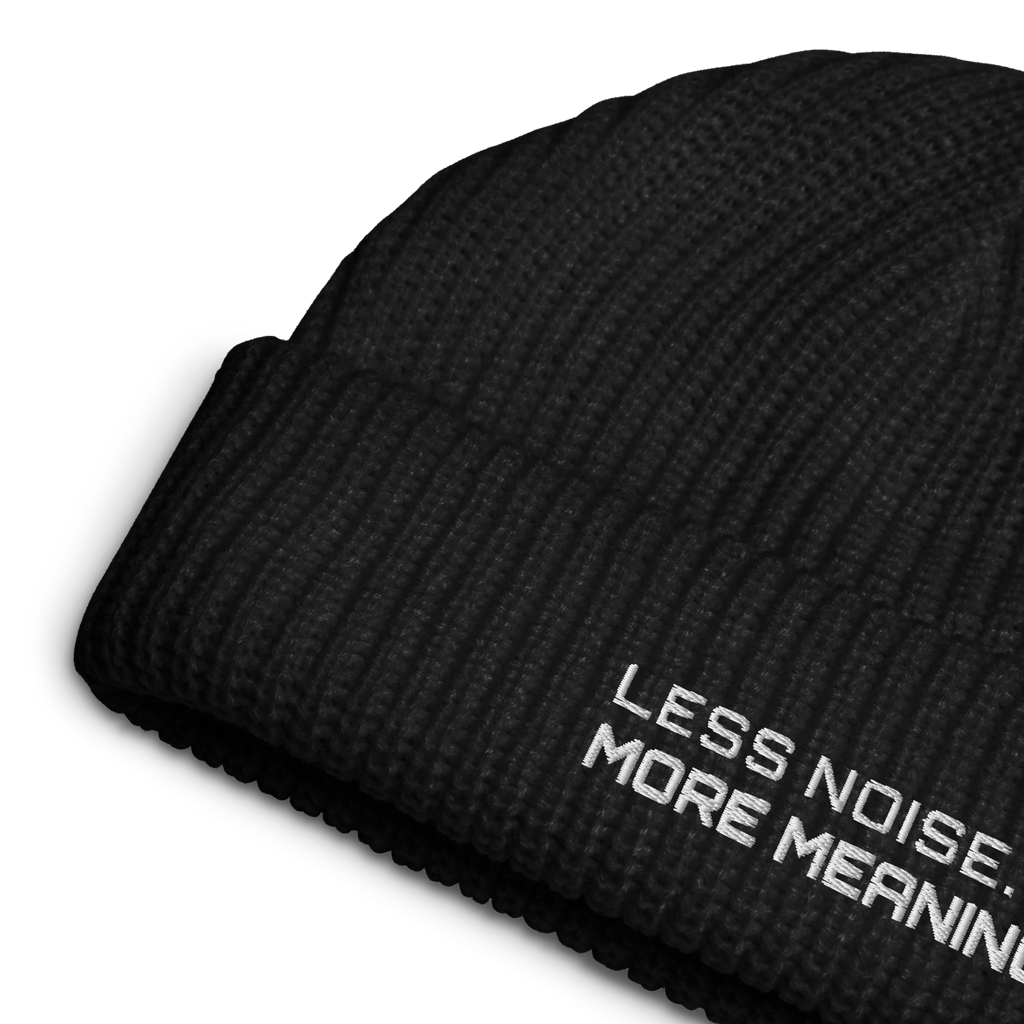 Black fisherman beanie close-up showing embroidered Less Noise More Meaning slogan