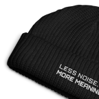 Black fisherman beanie close-up showing embroidered Less Noise More Meaning slogan