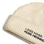 Ecru fisherman beanie close-up showing embroidered Less Noise More Meaning slogan