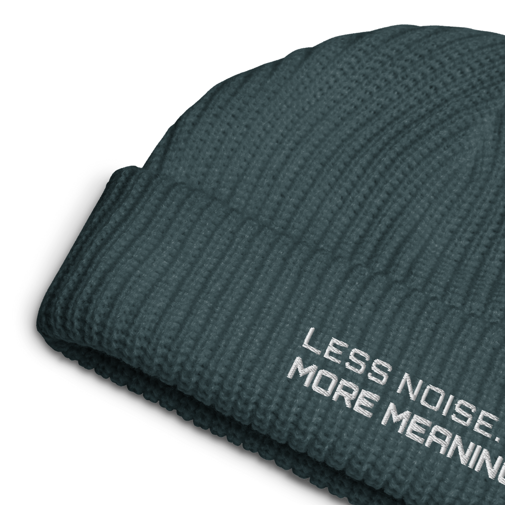 Petrol Blue fisherman beanie close-up showing embroidered Less Noise More Meaning slogan